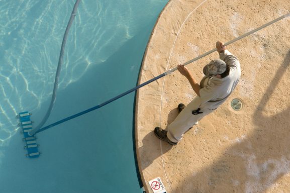 Ein Arbeiter reinigt den Rand eines Pools mit einem langen Schlauch.