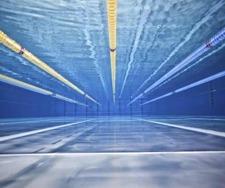 Blick auf einen Schwimmpool mit blauen Wasser und farbigen Bahnmarkierungen.